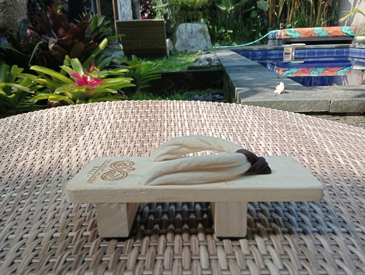 Wooden geta photographed poolside in Bali, surrounded by tropical foliage